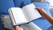 © yosaaa - Open blue book, blank pages, hands holding