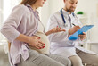 © Studio Romantic - Young pregnant woman having appointment with doctor. Future mother sitting in obgyn office and talking to pregnancy specialist. Woman who's expecting baby talking to male obgyn with clipboard