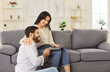 © Studio Romantic - Young cheerful couple sitting on sofa in living room at home together watching video or using laptop for internet and social media. Happy man and woman resting on couch enjoying weekend