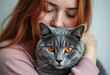 © Jeffrey - A woman gently hugs her beautiful grey domestic cat with striking orange eyes, showing deep affection and a loving pet bond.