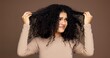 © peopleimages.com - Curly, hair and woman in studio with damage, frizz problem and dry texture on brown background. Hairdresser, salon and person with worry for haircare treatment, grooming routine and shampoo products