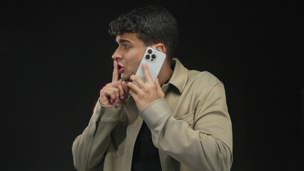 Man grabs phone while talking against background showing hispanic young male making mobile call on simple backdrop.