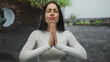 © Krakenimages.com - Young hispanic woman outdoors in peaceful natural setting wearing white attire, expressing calm with hands in prayer posture surrounded by greenery and stone architecture.