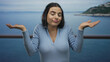 © Krakenimages.com - Woman in blue sweater gesturing uncertainty on seaside promenade with the ocean as background on a cloudy day.