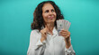 © Krakenimages.com - Middle-aged woman holding colombian pesos thoughtfully against a blue background, reflecting on finances and monetary value.