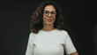 © Krakenimages.com - Woman smiling giving thumbs up in white shirt against dark background with curly hair glasses joyful confident isolated happy positive confident cheerful middle-aged hispanic