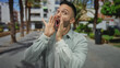 © Krakenimages.com - Young hispanic man shouting outdoors in a vibrant urban street with palm trees and city buildings creating a lively and dynamic urban setting.