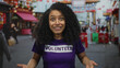© Krakenimages.com - Hispanic woman in volunteer shirt smiling energetically on a lively street, capturing the essence of community, engagement, and outdoor activities in an urban setting.