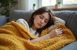 © miss irine - Young woman rests on gray couch with warm yellow blanket. She is relaxed, seated on furniture, head on soft blanket, seeking comfort and relief. Woman is surrounded by cozy interior.