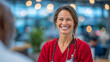 © Maksym - Red-scrubbed nurse shares a supportive glance with unseen patient, stethoscope hanging naturally, behind her the bustling clinic glows with collaborative energy and optimism