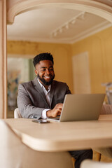 Portrait of smiling young businessman doing online research over laptop while sitting at desk in office