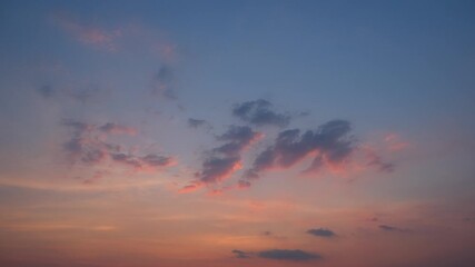 Wall Mural - A peaceful sunset sky timelapse with soft orange and pink light illuminating scattered dark clouds against a fading blue sky, creating a calm and soothing end to the day’s light. Time lapse.
