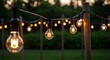 © Senja - String of illuminated Edison-style light bulbs hanging outdoors, creating a warm and inviting atmosphere in a garden setting.