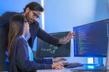 Asian female AI programmer and Indian male data analyst reviewing code on a monitor. Diverse tech professionals collaborating on an artificial intelligence project in a modern office.