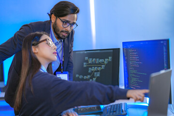 Asian female AI programmer and Indian male data analyst reviewing code on a monitor. Diverse tech professionals collaborating on an artificial intelligence project in a modern office.
