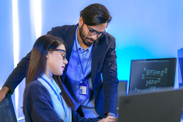Asian female AI programmer and Indian male data analyst reviewing code on a monitor. Diverse tech professionals collaborating on an artificial intelligence project in a modern office.