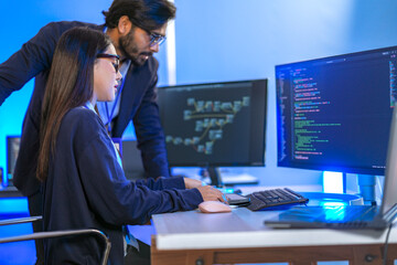 Asian female AI programmer and Indian male data analyst reviewing code on a monitor. Diverse tech professionals collaborating on an artificial intelligence project in a modern office.