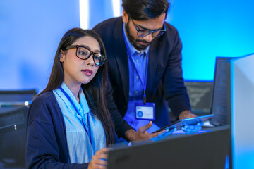 Asian female AI programmer and Indian male data analyst reviewing code on a monitor. Diverse tech professionals collaborating on an artificial intelligence project in a modern office.