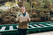 © mdyn - Tourist man studies map while on wooden pier by river. Traveler with backpack, planning outdoor adventure, hiking or climbing route.