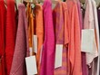 © RooM The Agency - Close-up of assorted pink, orange and red clothes hanging on a clothes rail for sale with blank tags in a shop