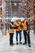 © Koldo_Studio - Warehouse workers wearing safety vests and helmets using barcode scanners and digital tablets, collaborating on inventory management within a large distribution center
