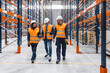 © Koldo_Studio - Warehouse workers wearing safety vests and hardhats are walking through large distribution center and discussing logistics