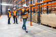 © Koldo_Studio - Warehouse manager using smartphone and holding clipboard is walking in a warehouse while workers are checking inventory