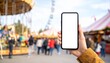 © idudung - Hand Holding Smartphone with Blank Screen at Amusement Park