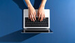 © Zulfa - Human Hands Typing on Laptop Overhead View Minimalist Blue Background Modern Digital Workspace