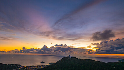 Wall Mural - Aerial hyper lapse view of A breathtaking sunset paints the sky in vivid hues of orange and blue over a coastal town, with lush green hills framing the scene. cloud in dramatic sunset over the ocean