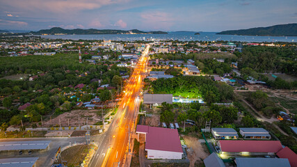 Wall Mural - Aerial hyper lapse view of A breathtaking sunset paints the sky in vivid hues of orange and blue over a coastal town, with lush green hills framing the scene. cloud in dramatic sunset over the ocean