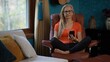 © Robert Peak - Portrait of unhappy, angry mature woman wearing glasses and an orange shirt sits in a brown leather chair. She is looking at her smartphone and at camera.
