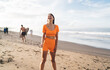 © BullRun - Brunette woman in bright orange outfit laughing joyfully on beach, radiating positivity and illustrating freedom from digital pressure through wellness-focused mindset.