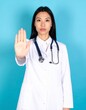 © Marliyana - Asian female doctor in lab coat gesturing stop sign against blue background