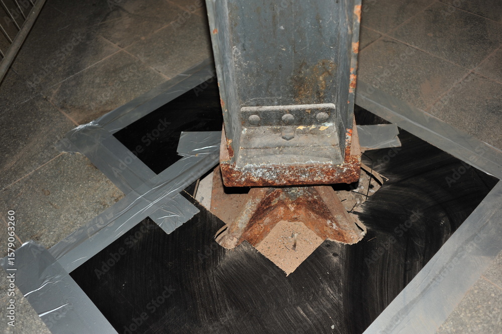 The base of a metal column is bolted to a concrete foundation. The ...