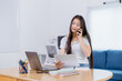 © Tj - Asian female freelancer working from home, managing her business, talking on the phone, and reviewing important documents while sitting comfortably at her modern desk, exuding confidence and focus