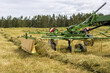 © Anastasija - Making hay with the hay tedder. Farm Machine Tractor With Rotating Rake Attachments. Close Up Shot. Tractor with tedder shaking mowed grass.