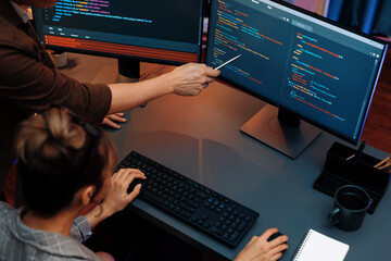 Top view of IT developers discussing with point to intelligent website development coder system running data online two screens information technology at neon light room at modern office. Infobahn.