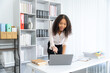 © Kritdanai - Office worker discovery: A young businesswoman leans over her laptop, a look of excited discovery on her face. Documents and office supplies surround her, highlighting a busy workspace.