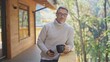 © nyul - Relaxed man drinking coffee using mobile phone on balcony of modern wooden house in mountains. Portrait of happy mature businessman enjoying nature and peaceful moment of vacation, smiling.