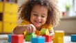 © Vadym - Happy toddler girl with curly hair plays with colorful wooden blocks. Joyful expression radiates pure curiosity, delight. Close-up shot focuses on innocent engagement, childhood development, learning