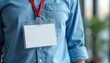 © Vadym - Red lanyard holds blank identification card on person wearing blue buttoned shirt. Clear plastic holder displays empty name tag. Professional accessory for business, office, event staff