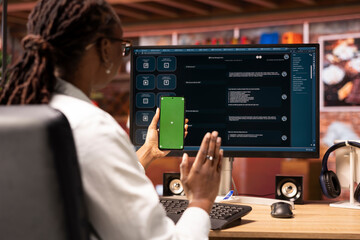 Woman greets friend during videocall on green screen phone in front of PC screen with AI LLM chatbot. Person waves hand, saluting mate during teleconference on mockup phone, using large language model