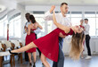 © JackF - Smiling young woman in elegant red clothes learn to dance couples latin dance, energetic and fast tango in modern dance salon
