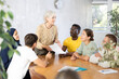 © JackF - Friendly aged woman conducting language speaking club, communicating with group of adults people of different nationalities gathered around table..