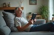 © Vadym - Senior man relaxes on sofa using tablet. Mature male with grey hair browses internet, connects online. Home comfort with digital device, enjoying wireless technology, retirement lifestyle.