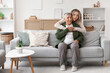 © Pixel-Shot - Young woman hugging her grandmother on sofa at home