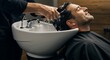 © mr. arsad - A client seated in a barber chair receiving a hair wash at a sink station, foamy shampoo and water droplets in detail, comfortable and relaxing,