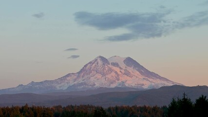 Wall Mural - aerial drone shot of mount rainier glowing at sunset with soft light on snow-capped peak and forest 