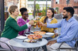 © sofiko14 - Group of friends enjoying a meal together outdoors, clinking glasses in a celebratory toast.